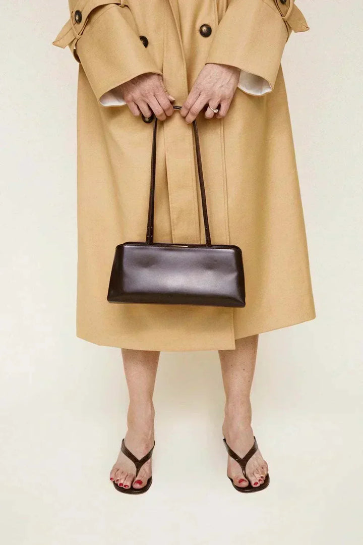 Sleek brown Leclair handbag with structured frame held by person in beige trench coat