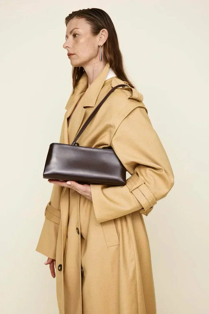 Woman wearing beige coat holding sleek black Leclair handbag with structured frame closure and elongated silhouette