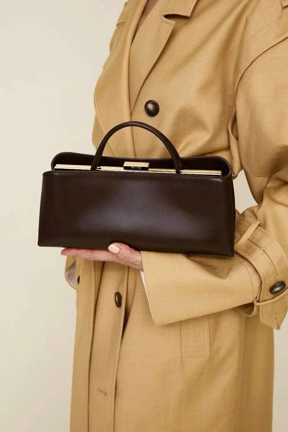 Elegant black Leclair handbag with structured frame held by person in beige coat