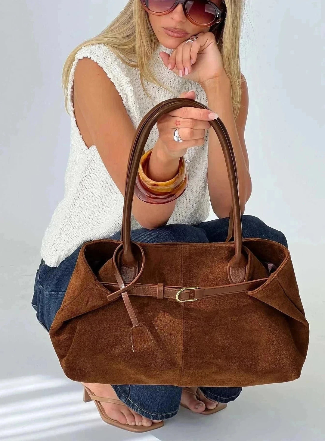 Brown suede tote bag with belted detail and soft structured silhouette held by woman