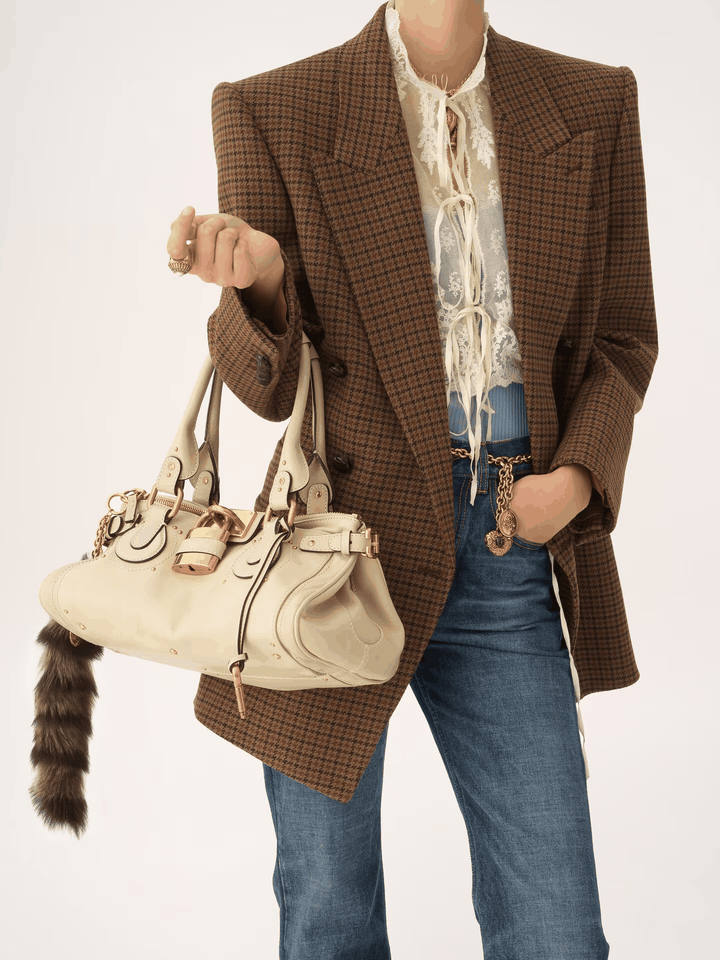 Marcelle Lock Handbag with oversized gold lock and double handles in smooth vegan leather, worn with brown check blazer and jeans