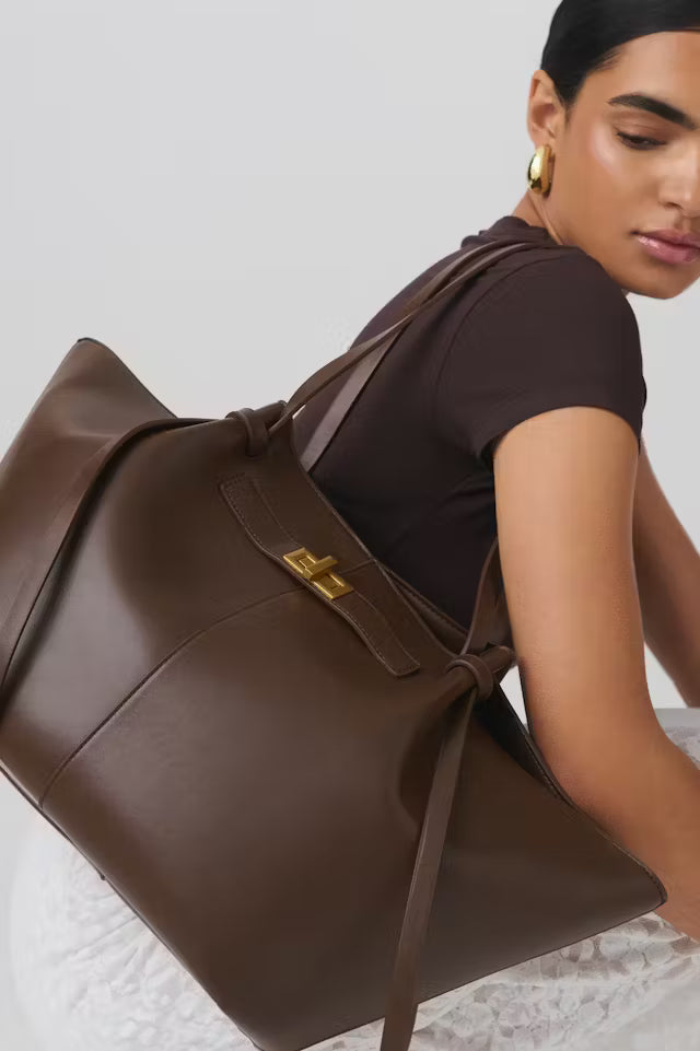 Brown Delair tote bag in vegan leather with gold clasp on model's shoulder