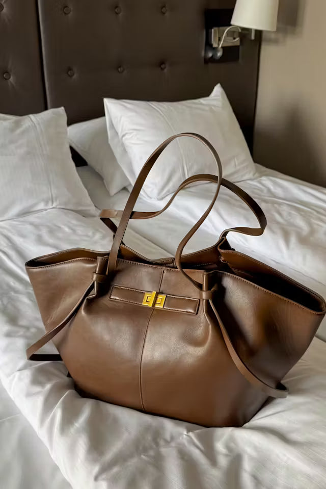Brown supple vegan leather Delair tote bag with gold buckle on bed