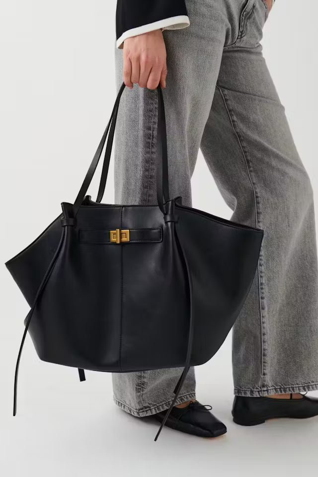 Black vegan leather Delair tote bag with relaxed silhouette and minimal detailing carried by person in gray jeans