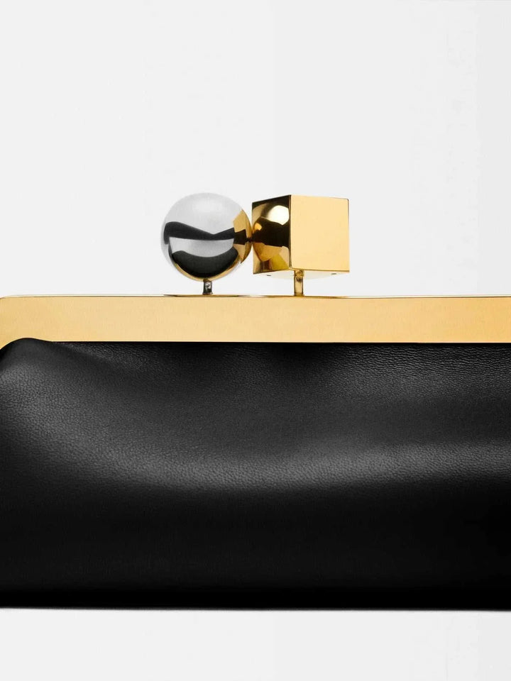 Black vegan leather clutch bag with gold frame and dual-metal clasp, sleek and sculptural design.
