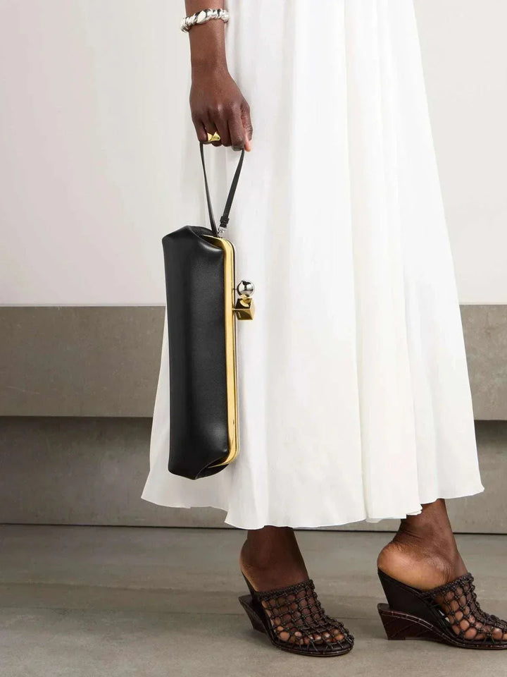 Sleek black clutch bag with bold gold frame and dual-metal clasp held by a woman in a white dress
