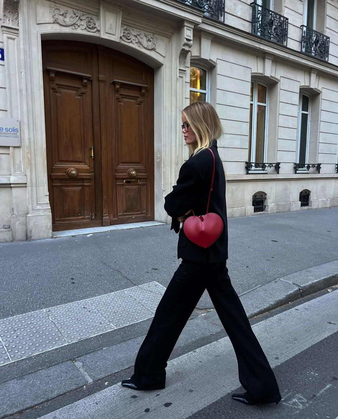 woman wearing a black outfit carrying a red 3D heart-shaped crossbody bag on a city street