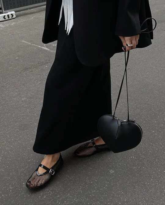 Black heart-shaped 3D crossbody bag in vegan leather with adjustable strap and knotted handles worn with black outfit