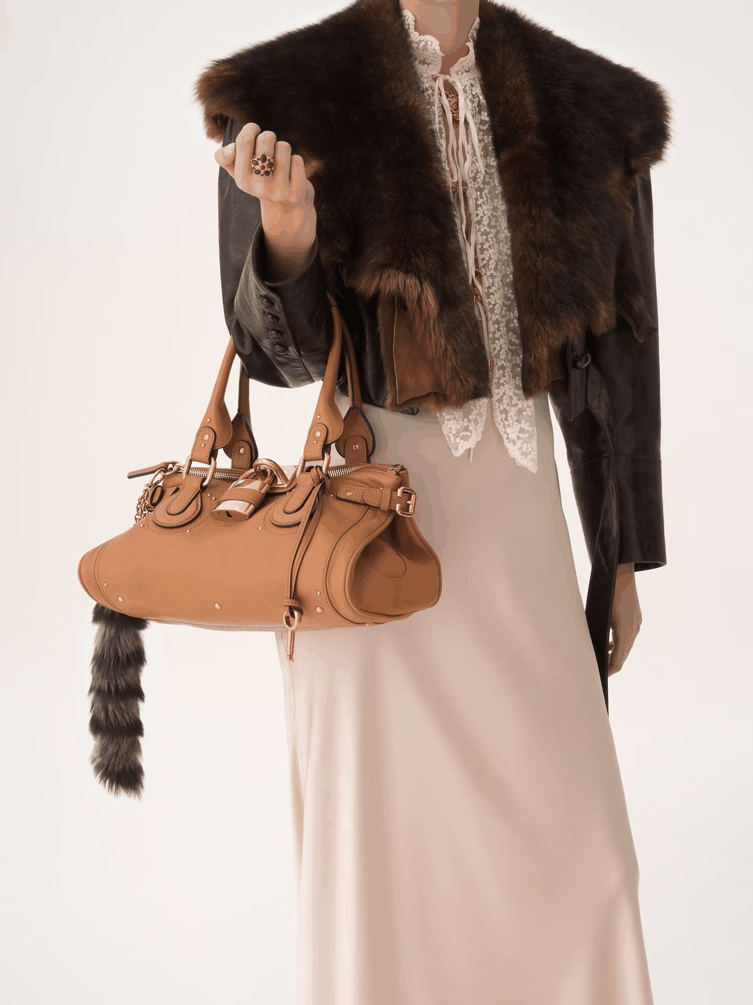 Marcelle Lock Handbag in smooth vegan leather with oversized gold lock and double handles, held by a model in vintage outfit