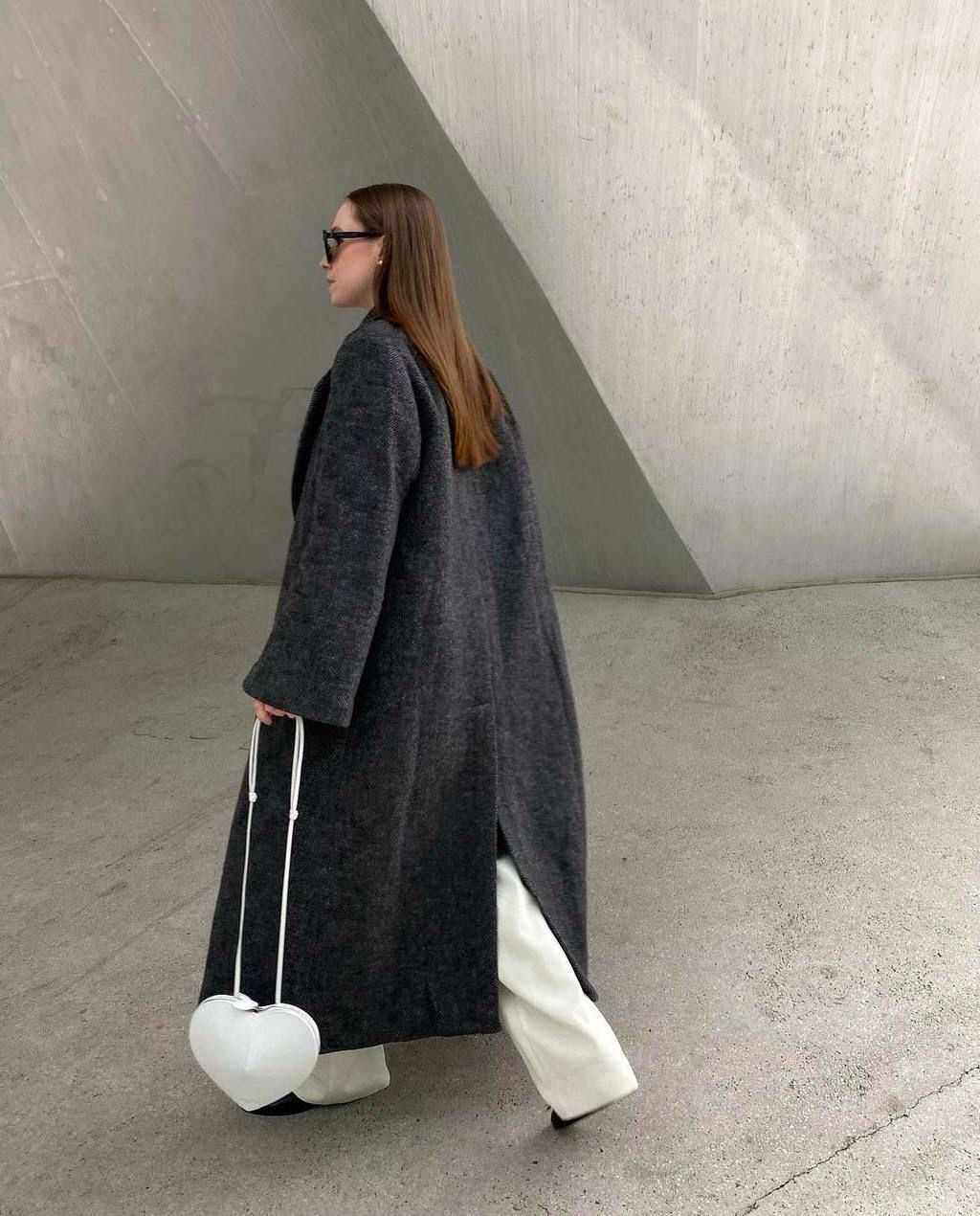 Woman wearing dark coat carrying white heart-shaped 3D crossbody bag with adjustable strap and knotted top handles