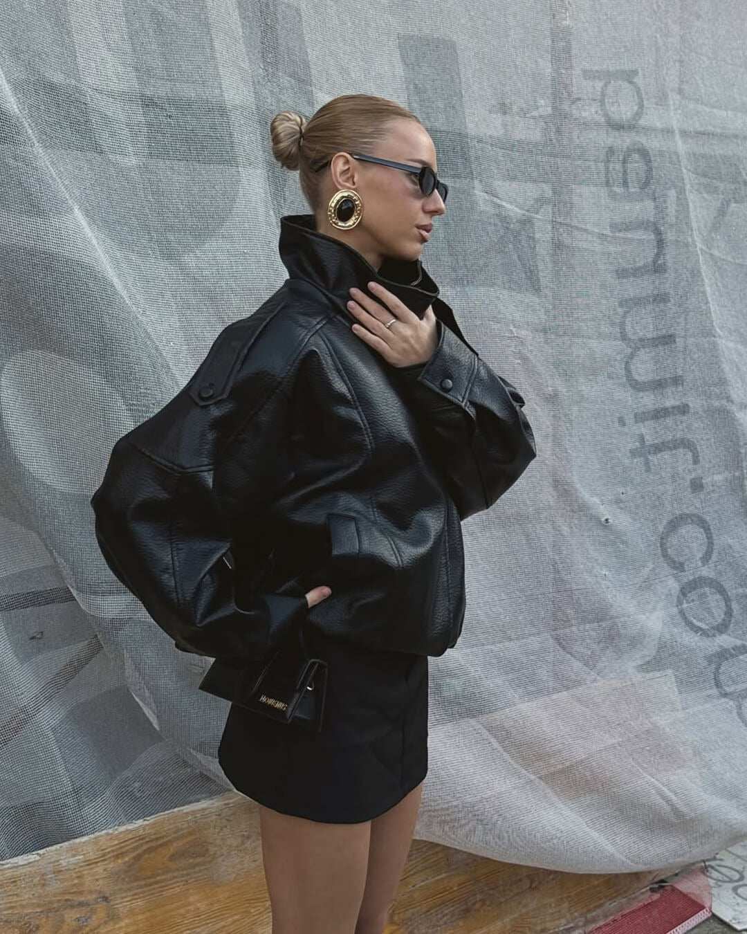 Oversized faux leather funnel neck jacket with asymmetrical front and elasticated hem worn by woman