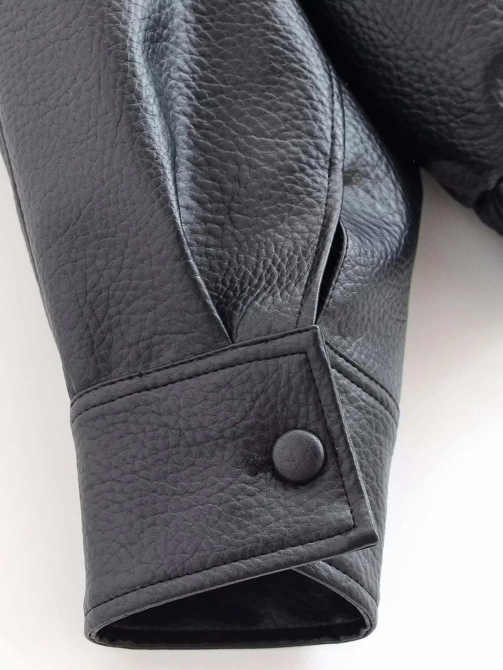 Close-up of textured black faux leather jacket sleeve with snap-button cuff detail and sculpted design.