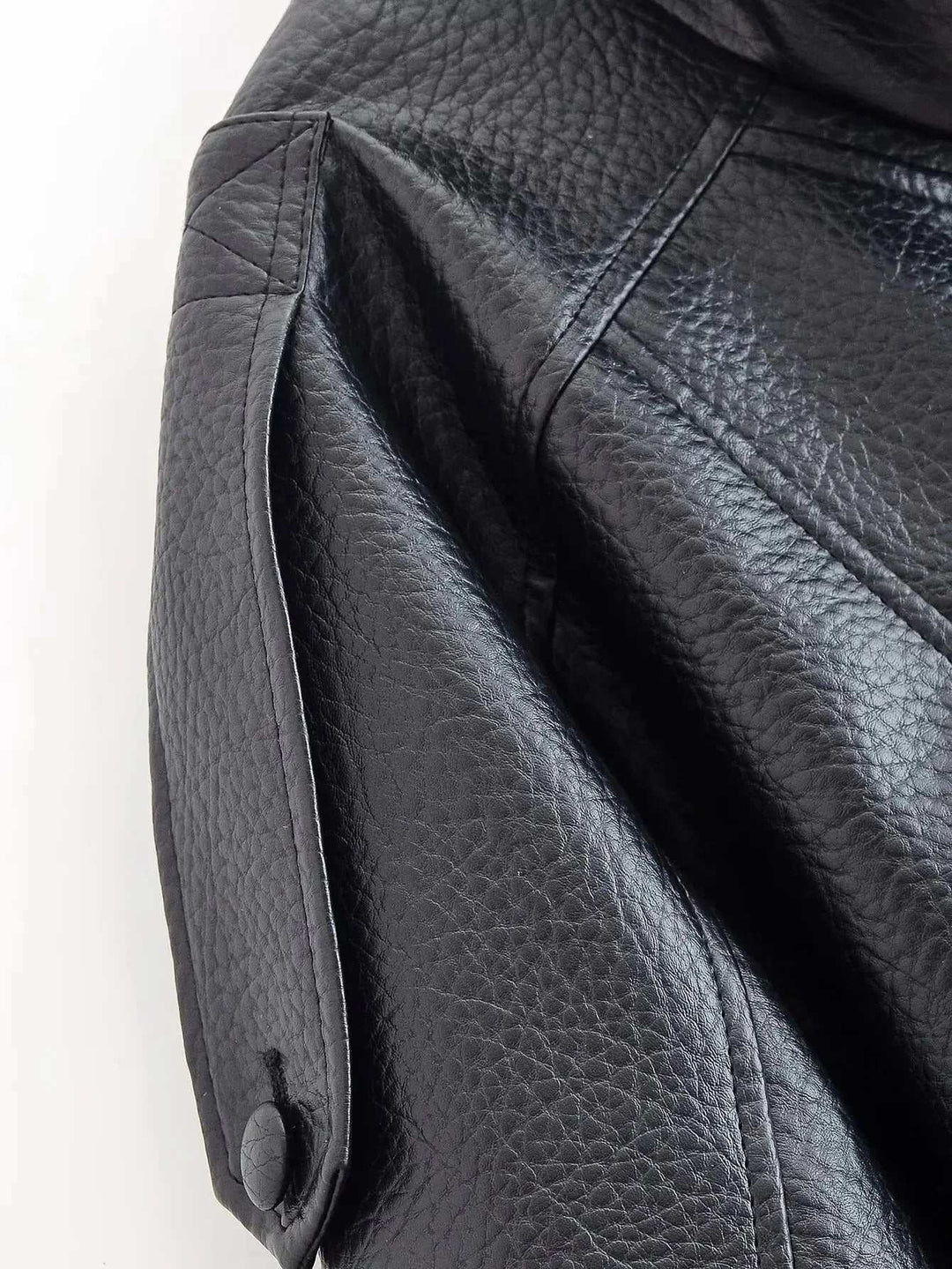 Close-up of black faux leather jacket sleeve with snap-button detail and textured leather funnel neck design