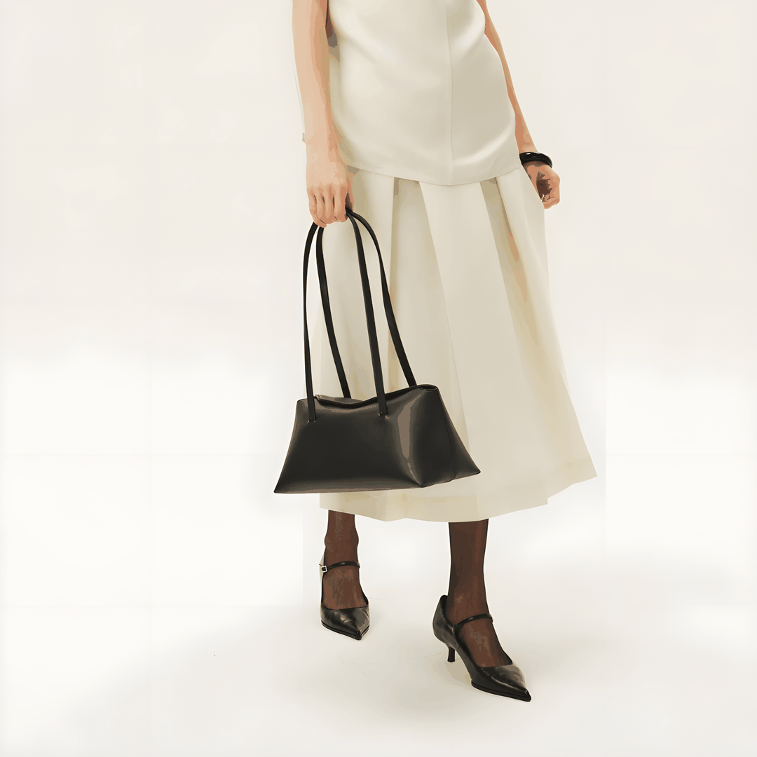 Elegant black Christelle shoulder bag in vegan leather with magnetic closure and dual straps, styled with white outfit and black heels.