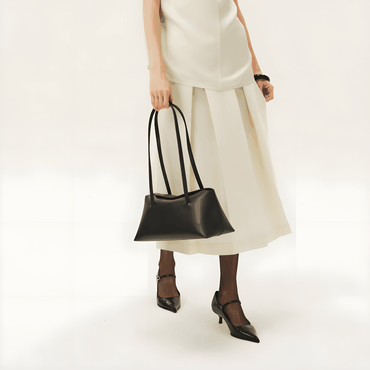 Elegant black Christelle shoulder bag in vegan leather with magnetic closure and dual straps, styled with white outfit and black heels.